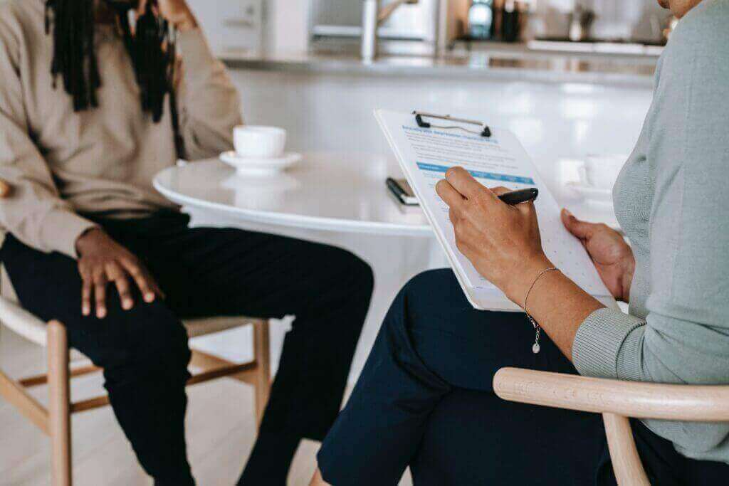 Picture of two people in conversation, the person in the foreground fills out a form, strategy, sound negotiator, negotiation, ai.